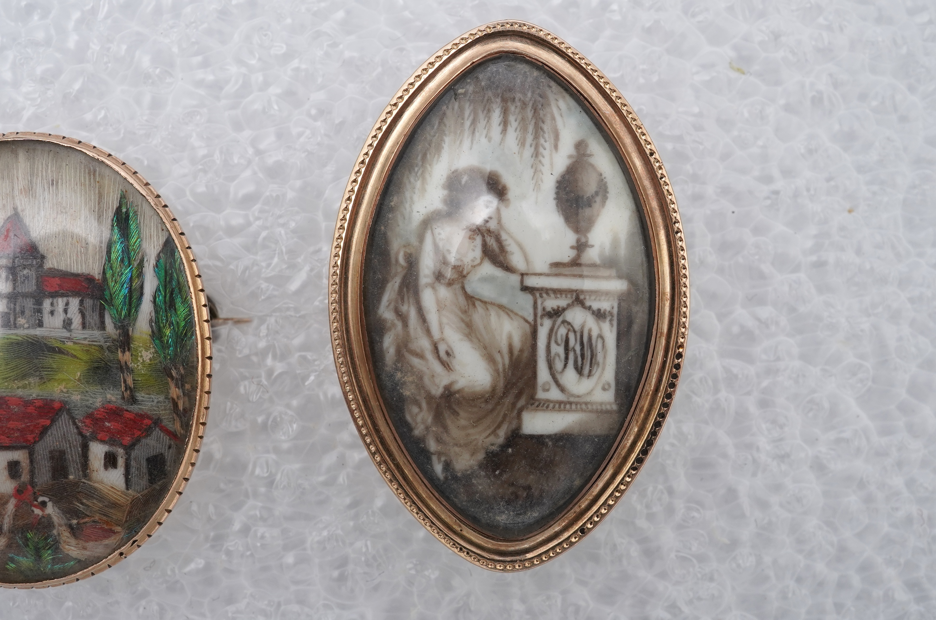 A George III ivory mourning brooch, circa 1786, and a feather work brooch, 19th century